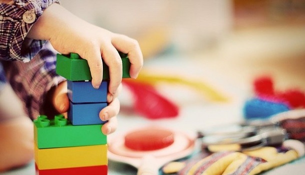 Das Bild zeigt Kinderhände, welche einen Turm aus bunten Bausteinen bauen